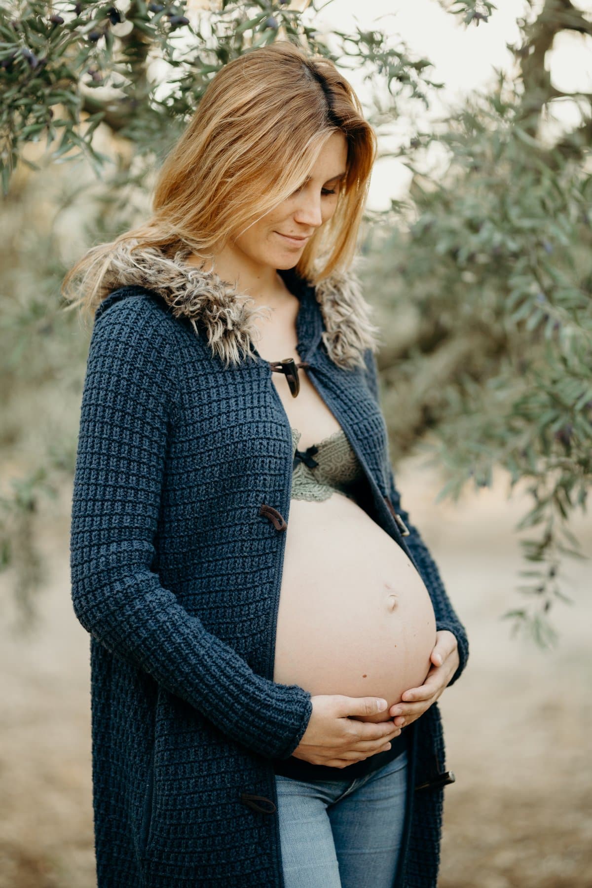 Femme enceinte sous les oliviers, mains sur son ventre, séance photo grossesse