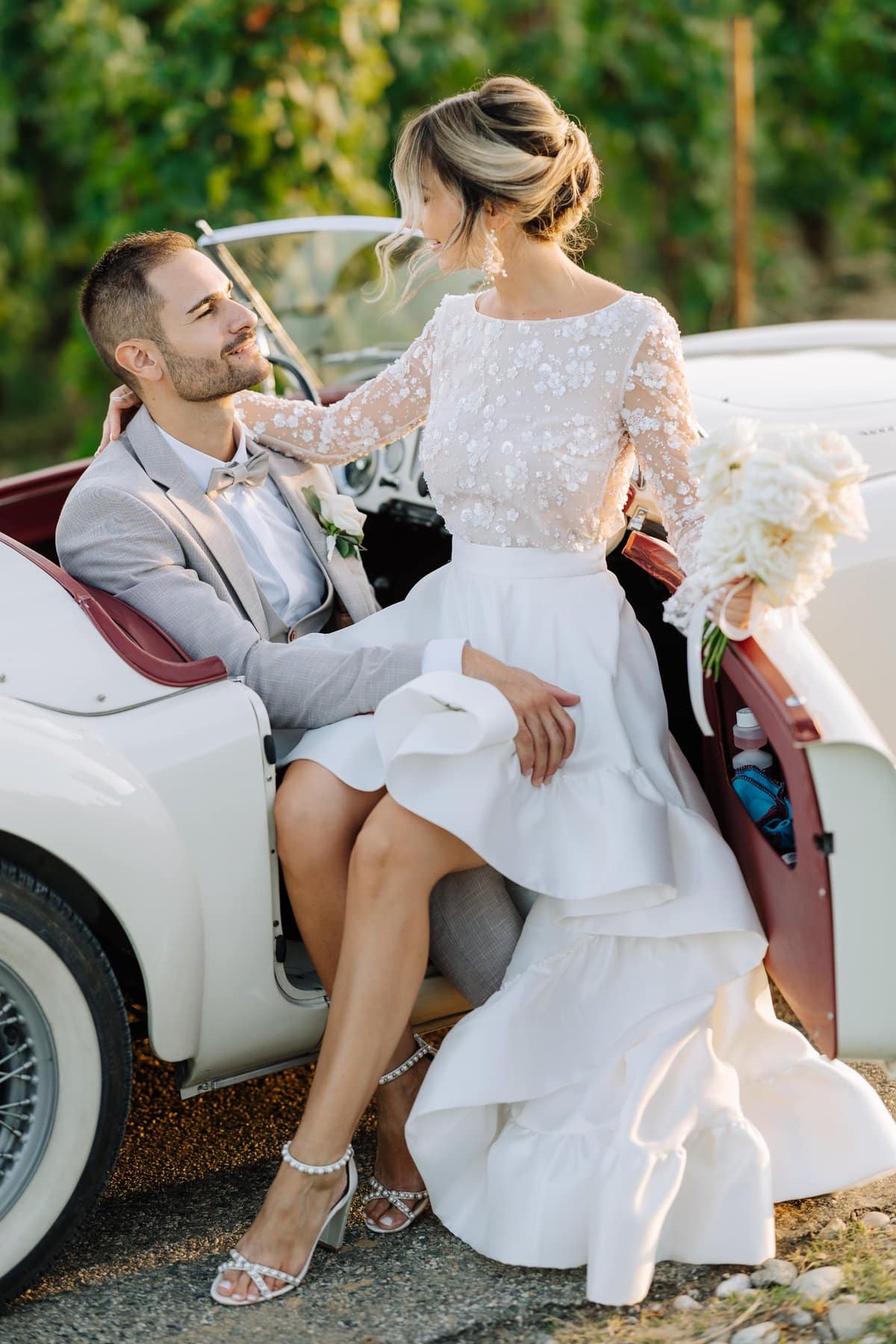 Mariée assise sur une voiture ancienne aux côtés du marié