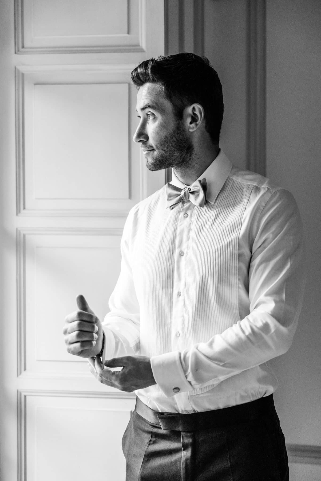 Marié ajustant sa chemise près d'une fenêtre pendant les préparatifs du mariage